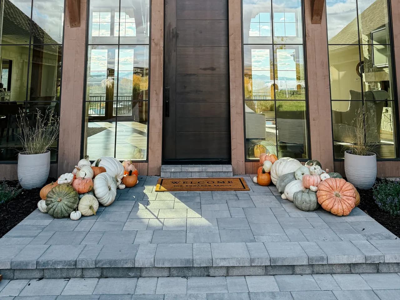 Modern timber home with sage, cream, and blush pumpkins flanking the entry in a muted palette