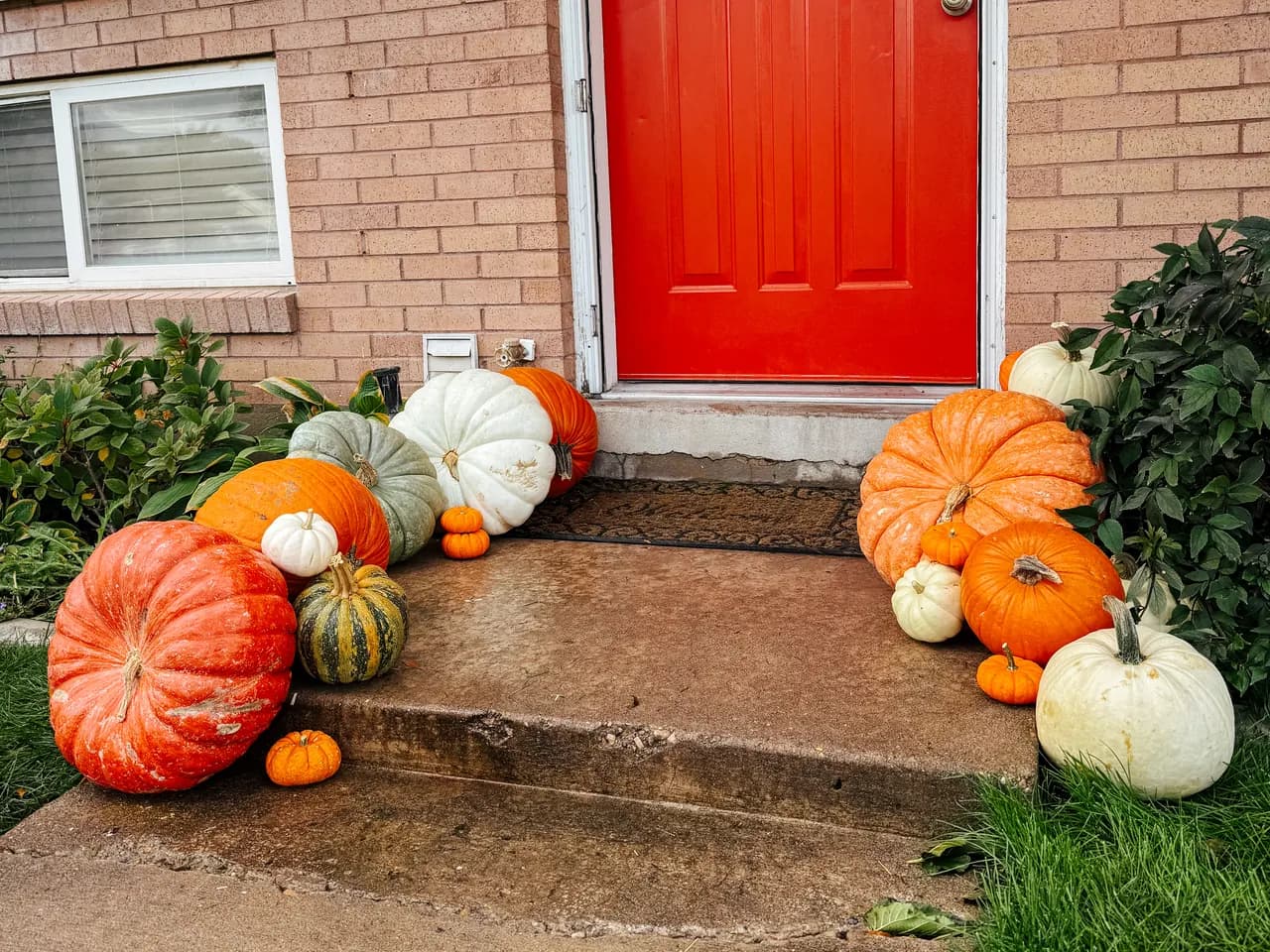 Red door brick home with classic autumn pumpkin arrangement flanking the stoop