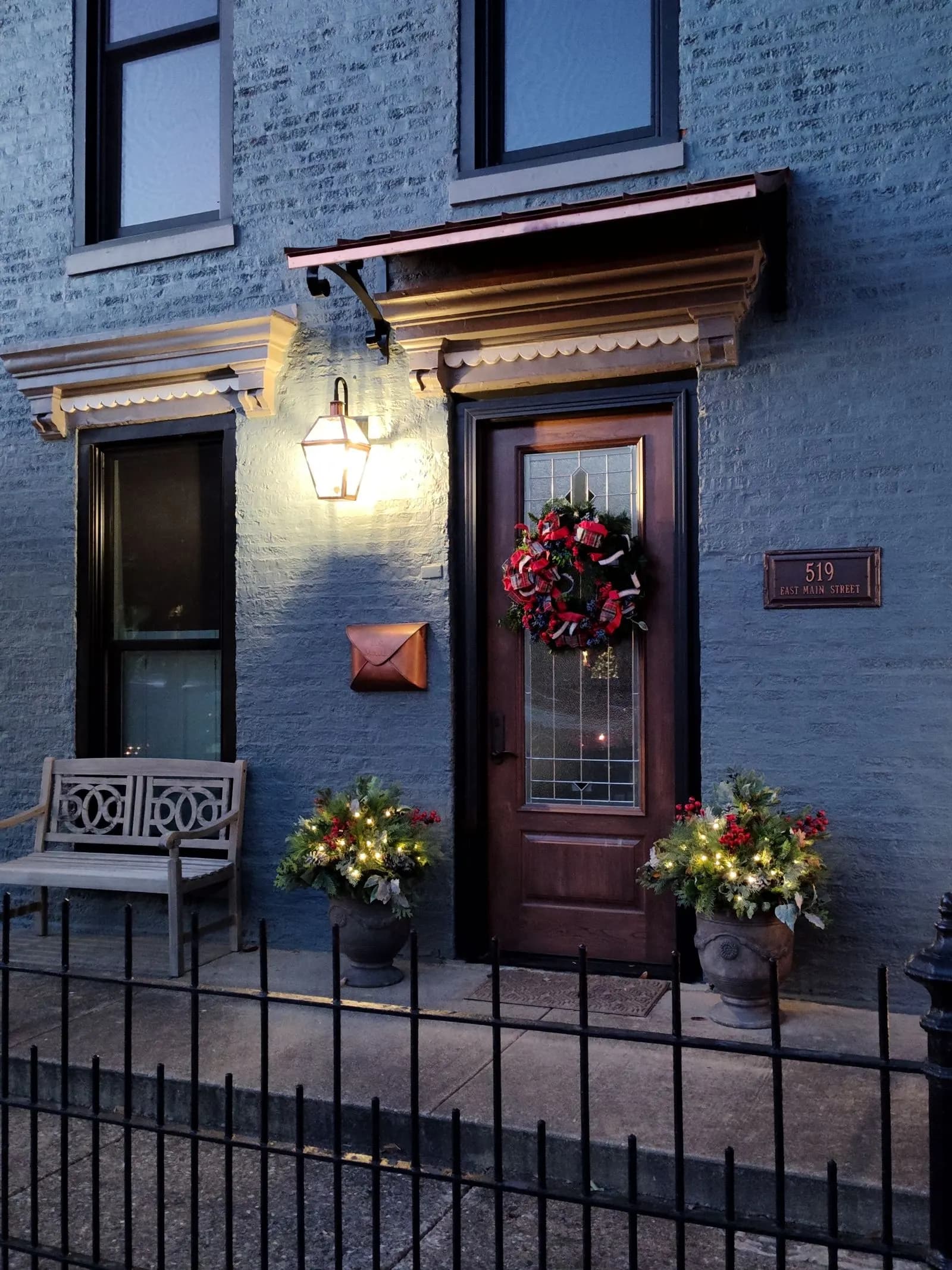 Front door with an evergreen wreath, lit planters, and a copper lantern glowing at dusk